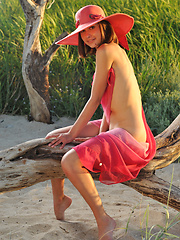 Enchanting girl in a hat with a wide brim showing her perfect body outdoor on the coast.